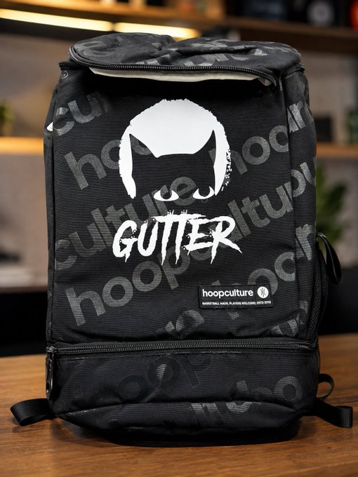 Black 'GUTTER' branded backpack by hoopculture featuring a white silhouette logo, displayed on a wooden surface.