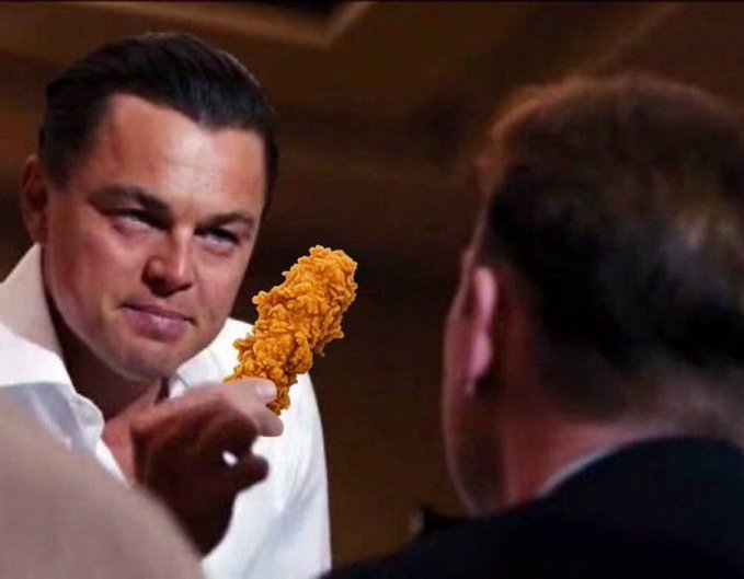 Leonardo DiCaprio, in character as Jordan Belfort from *The Wolf of Wall Street*, smirks while holding out a fried chicken tender toward another man, visually parodied to humorously suggest he is "hawking" chicken tendies as a hot stock tip. The meme plays on the slang "tendies" (used in investing communities to refer to profits) by literally showing the fried chicken treat, tying the image to the promotional post about the supposed ticker $tendies.