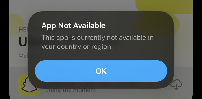 A smartphone screen displays a pop-up dialog stating 'App Not Available. This app is currently not available in your country or region.' with an 'OK' button, partially overlaying the Snapchat app interface.