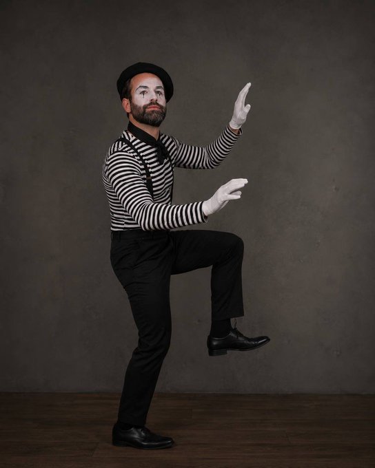 A bearded mime in a black-and-white striped shirt, black hat, suspenders, and white gloves strikes an exaggerated pose with one leg lifted and hands gesturing, embodying the theatrical absurdity of "Life after you take a Rainbet sponsorship." The performer's dramatic flair and over-the-top posture humorously play on the post's implication of comedic, scripted behavior that follows taking on the sponsorship.