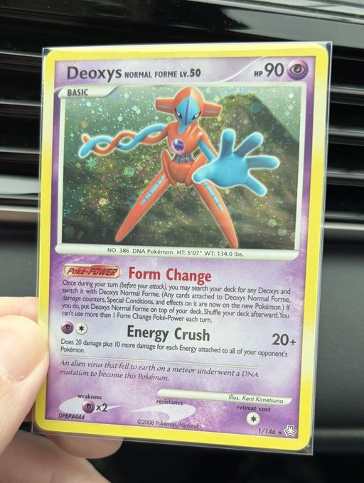 A hand holds a Pokemon trading card featuring Deoxys Normal Forme, a Psychic-type with 90 HP, displaying attacks 'Form Change' (Poké-POWER) and 'Energy Crush' (20+ damage). The card is numbered 1/146 and was illustrated by Ken Sugimori.