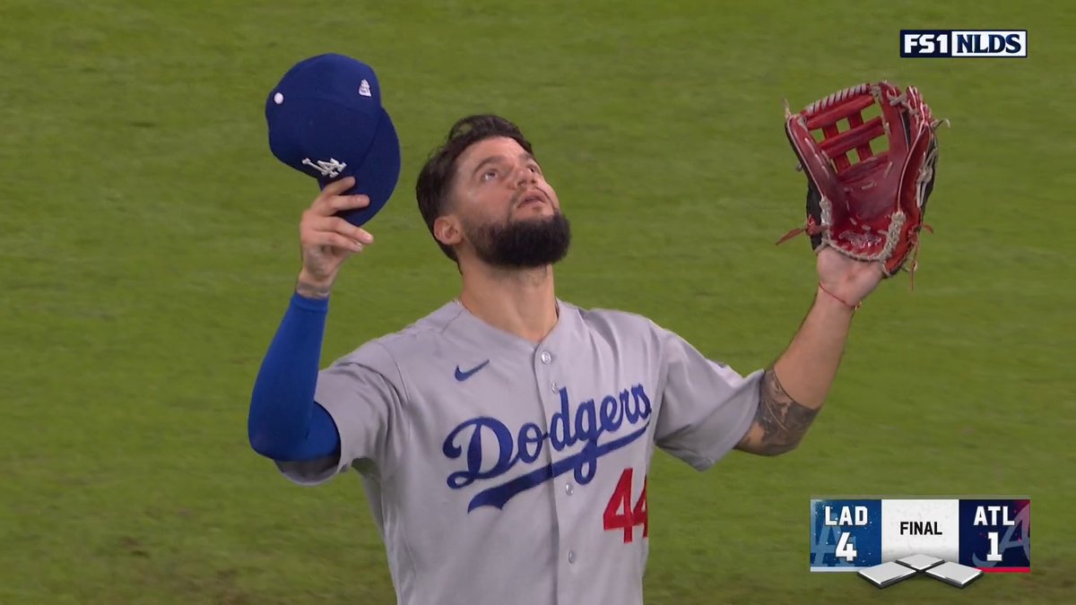 A Los Angeles Dodgers baseball player (#44) holds his hat and glove up toward the sky, with an FS1 NLDS graphic showing the Dodgers defeated Atlanta 4-1.