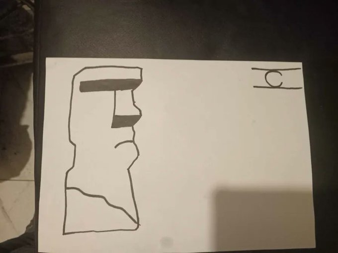 A photograph of a crude black marker drawing on white paper depicting a basic moai statue profile, with the letters 'HC' boxed in the top right corner, resting on a dark surface.