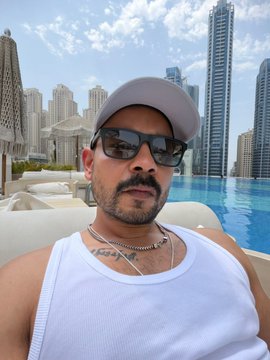 A man wearing a cap, sunglasses, and a white tank top takes a selfie by a rooftop pool with a city skyline in the background, capturing the relaxed Friday vibe mentioned in the post about Bitcoin ("$BTC").