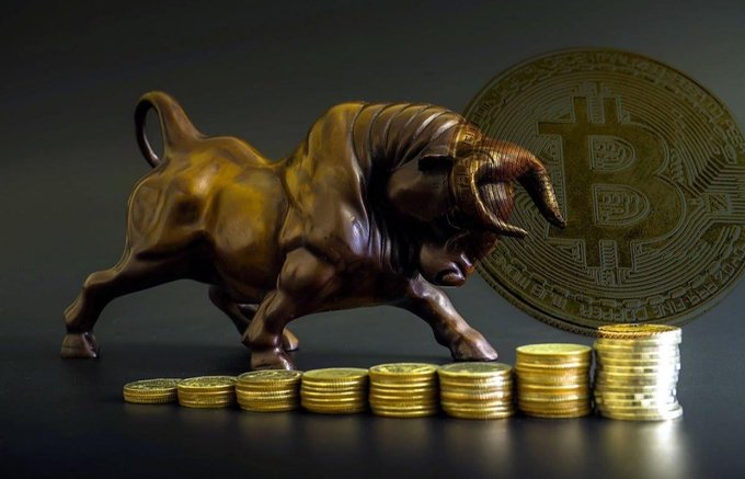 A bronze bull figurine charges forward against a large Bitcoin coin emblem with ascending stacks of gold coins arranged in a rising pattern at its feet, symbolizing Bitcoin's resilient climb past the $65K level and renewed bullish momentum from recovering spot ETF inflows and institutional demand.