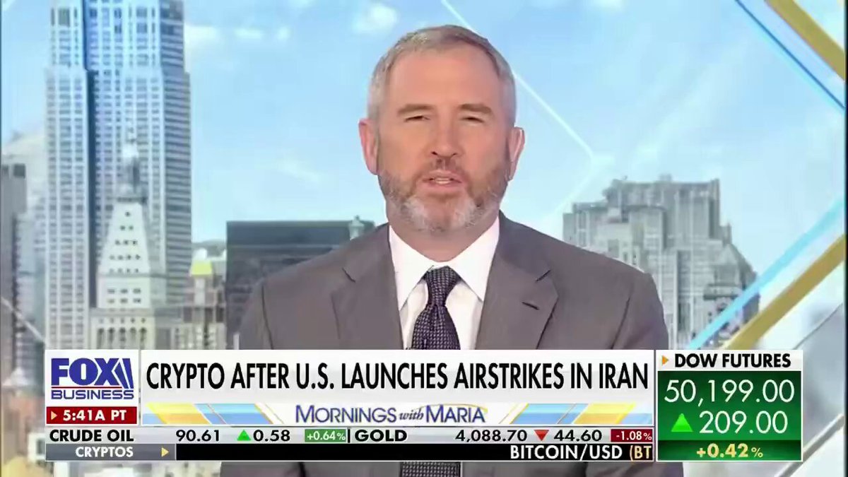The image shows a man wearing a suit, sitting at a desk with a TV screen behind him. The TV screen displays an interview with a man named Brad Garlinghouse who is talking about Bitcoin and cryptocurrency markets. The focus of the interview seems to be on the recent launch of cryptocurrencies in Iran. The post related to this interview highlights that Brad Garlinghouse has just launched his own cryptocurrency, Bitcoin, which he says will change the world for the better.