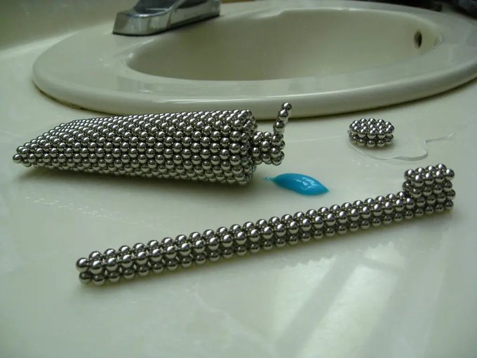Three cone-shaped objects constructed from small metallic magnetic balls sitting on a bathroom sink counter, with a small blue tag visible.