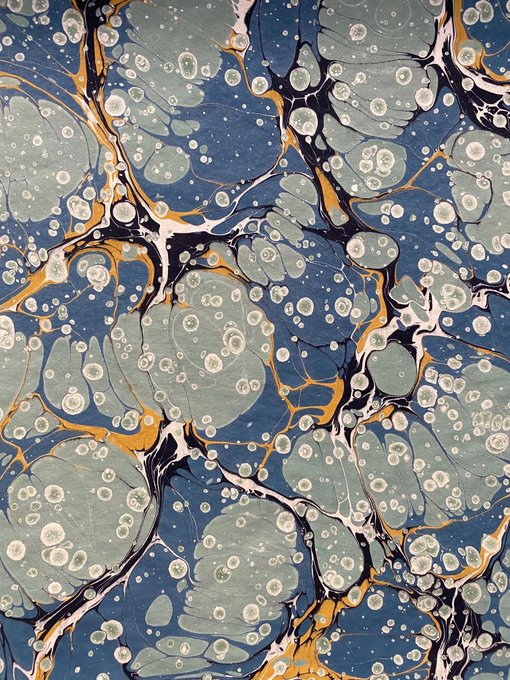 Abstract marbled art pattern featuring blue, gray, and white circular formations with black and gold veining throughout.