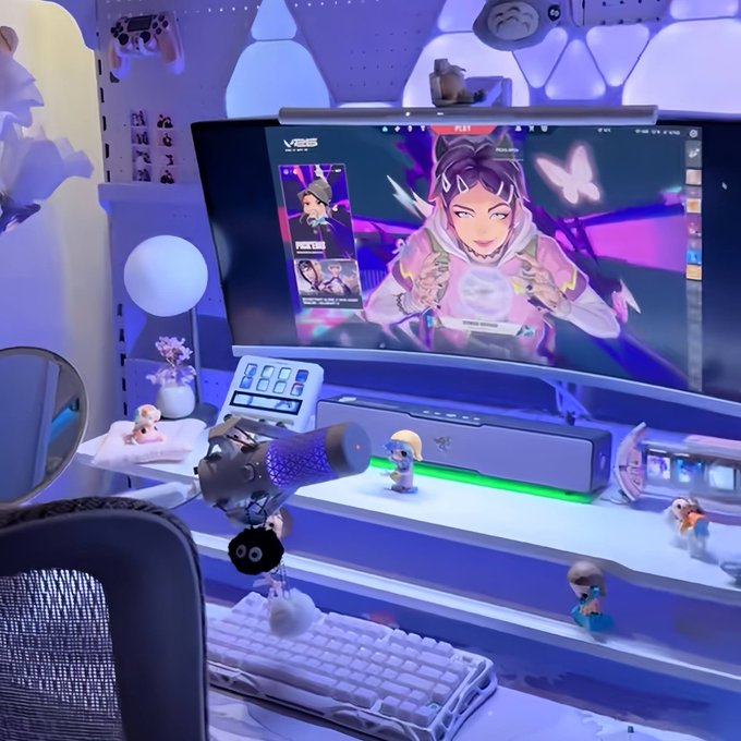 A gaming setup featuring a curved monitor displaying the Valorant character Clove, with RGB lighting, figurines, and decorative items on the desk.