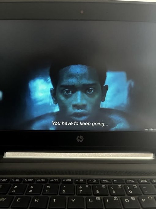 A laptop screen displays a movie scene of a sweaty, distressed-looking man with the subtitle 'You have to keep going...', with 'mobiletv' watermarked in the corner.