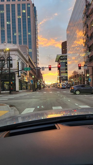 The image shows a city street with tall buildings, including one that appears to be a hotel or apartment building. There are several cars driving down the street at various times of day, indicating an active urban environment. The sun is setting behind these buildings, casting a warm glow over the scene and creating a beautiful backdrop for the photograph.

The image also contains text that reads "GM if you GM". This could be a caption or a tagline related to the photo, possibly referencing the photographer's name or the subject of the picture. The presence of this text suggests that it might be an advertisement or promotional material for a product or service, aiming to capture the viewer's attention and convey information about the image.