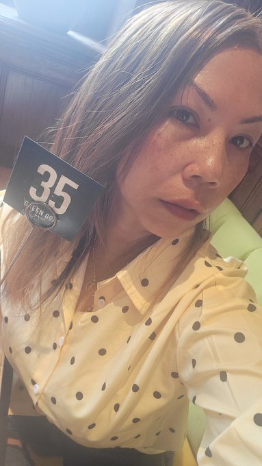 A woman with freckles wears a cream-colored polka dot blouse and holds a black card with '35' and 'GOLDEN GO' printed on it.