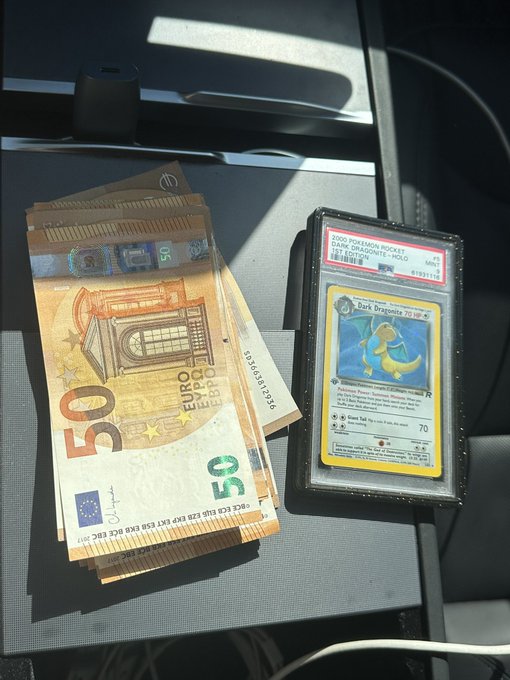 A fanned-out stack of 50 Euro banknotes rests on a car seat next to a graded PSA 9 Mint Dark Dragonite Pokémon card (2000 Wizards Rocket Deck), the cash and collectible shown together illustrating a completed sale transaction.