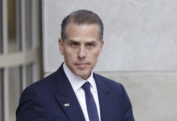 The image shows Hunter Biden, son of U.S. President Joe Biden, wearing a dark navy suit, white shirt, and tie, standing outside what appears to be a government building. The image relates to the post about the "$LAPTOP" meme token allegedly associated with Hunter Biden, which crashed more than 90% within 30 minutes of launch, losing over $106 billion in paper value.