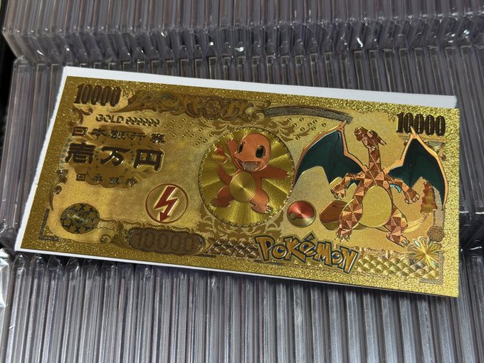 A gold-colored novelty banknote designed to resemble Japanese currency features Charmander and Charizard from Pokémon, with "10000" denominations, Japanese characters, and a lightning bolt logo set against a ridged metallic background, playfully styled as the "next Monkey Coin" with the contract address 0x1b1ddf2ddcd3d03c3ab3eb066c1f9a2d24bb7777 displayed on the front.