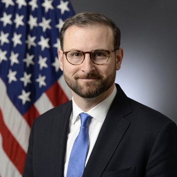 A man with glasses, a beard, and a blue tie stands in front of an American flag in what appears to be an official portrait.

The image relates to the post by depicting Patrick Witt, the White House crypto adviser mentioned in the article about the Trump administration's continued push for crypto legislation following the Clarity Act's failed Senate vote.