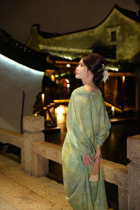 A woman in a flowing green traditional-style robe stands by a stone railing at night, gazing toward an illuminated building in the background, her hair adorned with white flowers.

The image evokes the elegance and innovation of a new era, visually paralleling Binance's promise of a refined, next-generation trading experience.