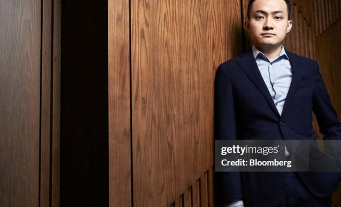 The image features a man dressed in a suit, standing against a wooden wall with his hands in his pockets. The photo has been edited to include text that reads "Governance and Community: Justin Sun’s Open Invitation Justin Sun repeatedly invites the community to participate in TRON’s governance and ecosystem development." This suggests that the image is related to a post about innovation, leadership, or community involvement within the context of TRON.