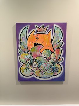 A colorful painting on a white wall featuring a crowned orange fox-like character surrounded by pastel cloud-like shapes with small creatures, set against a purple background.