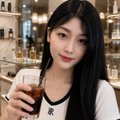 A selfie-style photo of a young Asian woman with long dark hair, wearing a dark top, holding a drink and smiling at the camera in what appears to be a restaurant or bar setting.