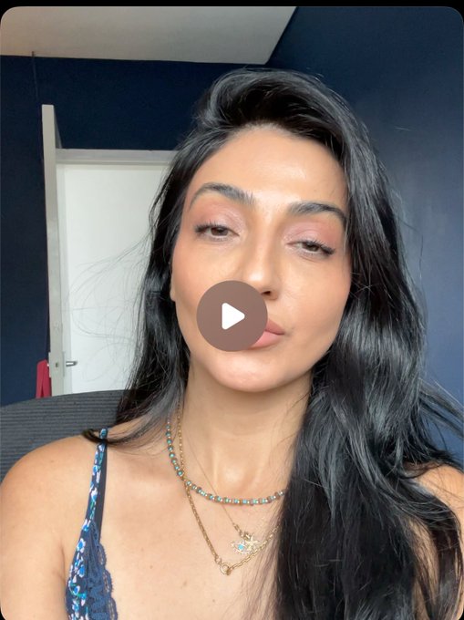 A woman with long dark hair wearing a beaded necklace and a blue lace top looks directly at the camera, with a play button overlay suggesting this is a video thumbnail. The image appears to be a self-introduction for a creator sharing insights from observing top memecoin traders on Solana and Robinhood.