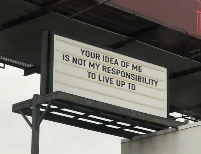A photograph of a billboard with the text 'YOUR IDEA OF ME IS NOT MY RESPONSIBILITY TO LIVE UP TO'.