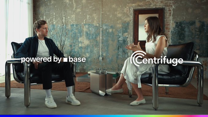 Two people sit in modern chairs having a conversation in a rustic room, with overlaid text reading 'powered by base' and 'Centrifuge' along with a colorful gradient bar at the bottom.