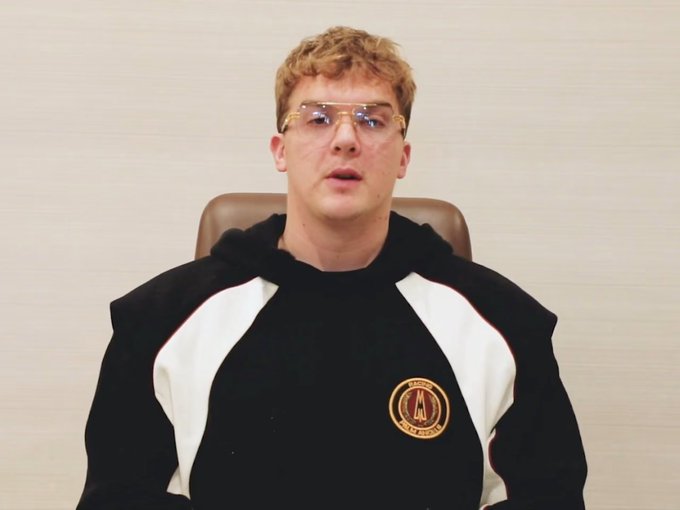 A young man with blonde hair and gold-rimmed glasses sits in a brown leather chair wearing a black and white hoodie featuring the Atlanta United FC logo, possibly referencing the "LIBRA: $1" token mentioned in the post.