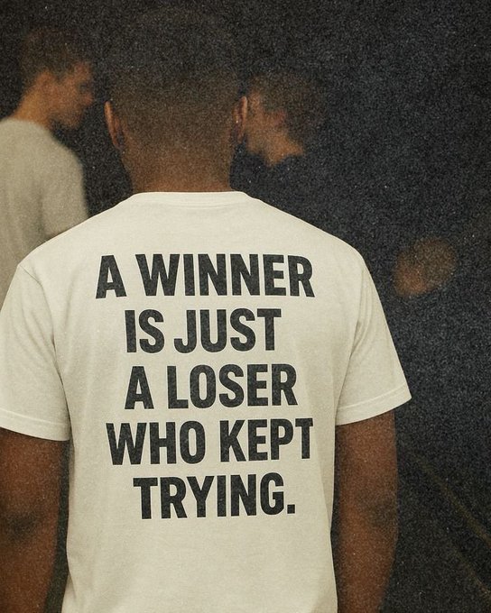 The back of a person wearing a white t-shirt is shown, with bold black text reading 'A WINNER IS JUST A LOSER WHO KEPT TRYING.'