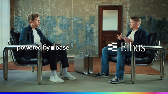 Two men sit in black chairs facing each other in an industrial-style room, with on-screen text reading "powered by base" and "Ethos".