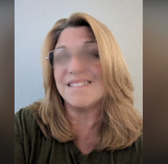 A close-up selfie of a woman with shoulder-length blonde hair and clear-framed glasses wearing an olive green shirt, with her eyes blurred for privacy.