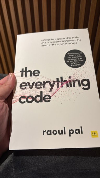 A hand holds up the book "The Everything Code" by Raoul Pal, with the subtitle "seizing the opportunities at the end of economic history and the dawn of the exponential age."