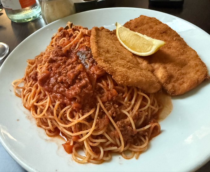 A plate of spaghetti bolognese served with a breaded cutlet and a lemon wedge garnish, presented as a hearty dinner. The image doesn't visually contain any text, numbers, or references to Solana, but the accompanying post contrasts the homemade meal with an optimistic $3 price target for SOL.
