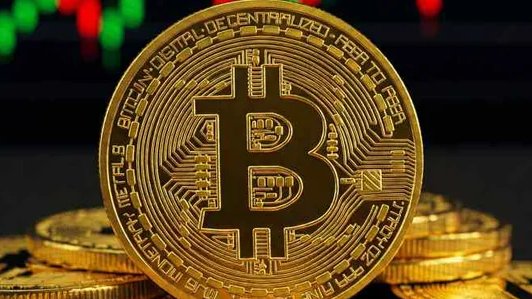 A close-up of a physical gold Bitcoin coin resting on other coins with a stock market chart in the background.