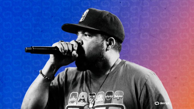 A man wearing a cap and graphic t-shirt holds a microphone close to his mouth against a blue and purple gradient background, with a 'decrypt' logo in the corner.