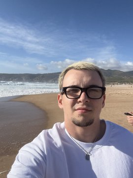 The image features a man wearing glasses, standing at the edge of a beach near the ocean. He appears to be posing for a photo while looking directly into the camera. The background shows the vast expanse of the ocean meeting the sky, creating an idyllic and serene setting. There is also text in the image that reads "gm gm CT Ready to buy wine with $BTC". This suggests that the man might be interested in purchasing some wine from a nearby winery or vineyard.