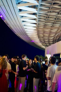 A crowd of people network under a striking, futuristic curved roof structure at night, illuminated by purple lighting—capturing the upscale, high-energy atmosphere of MoonPay's upscale events. The image visually represents the vibrant conference and experiential marketing environment the new Events & Marketing Manager would help orchestrate.