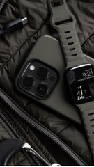 An olive green iPhone in a protective case resting on dark fabric alongside a smartwatch with green band displaying '35' (likely seconds) on its dark screen.