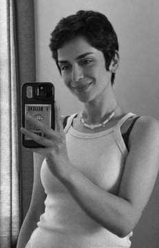 A black-and-white mirror selfie shows a smiling young woman with short dark hair holding up a smartphone to capture her reflection, complementing the post's theme of self-expression by framing her own image as a personal work of art.