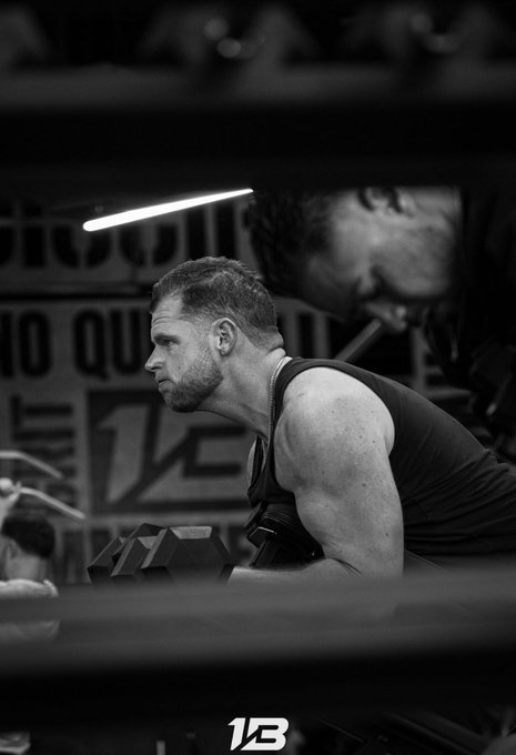 A focused athlete prepares with a dumbbell in hand inside a boxing ring, his intense gaze locked forward as he channels a "Lock in" mindset during his training session.