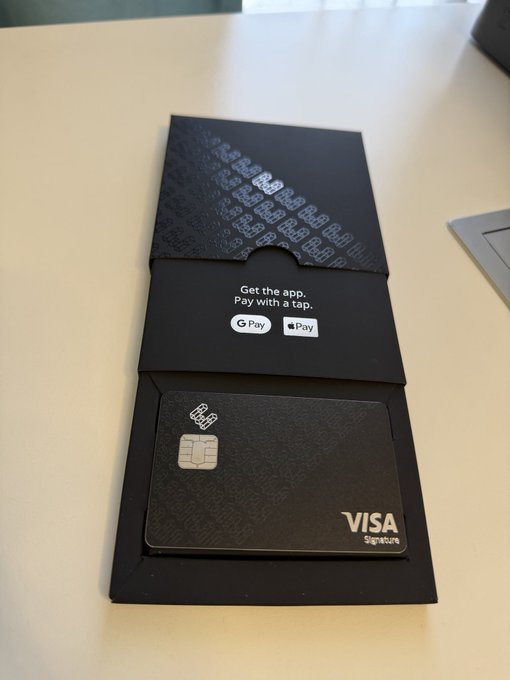 A photo of a black Visa Signature metal credit card with an accompanying card sleeve that reads 'Get the app. Pay with a tap.' alongside Google Pay and Apple Pay logos.
