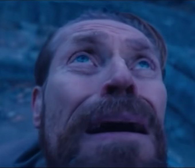 A close-up of a man with a mustache and beard looking upward with an emotional expression in a dimly lit scene.