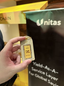 A hand holds a miniature gold bar keychain labeled "PLUS ULTRA" in front of a Unitas banner advertising a "Yield-As-A-Service Layer For Global Savings" at BNB Chain Tokyo, where Unitas is giving away gold bars amid Japan's strong crypto enthusiasm.