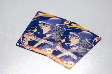 Two identical anime-style collectible cards featuring a character with silver hair, purple hat, and a rifle against a dark blue patterned background.
