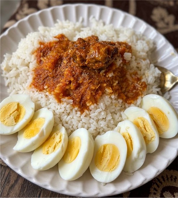 A plate of rice topped with a spicy red curry chicken dish, served with sliced boiled eggs arranged around the edge.
