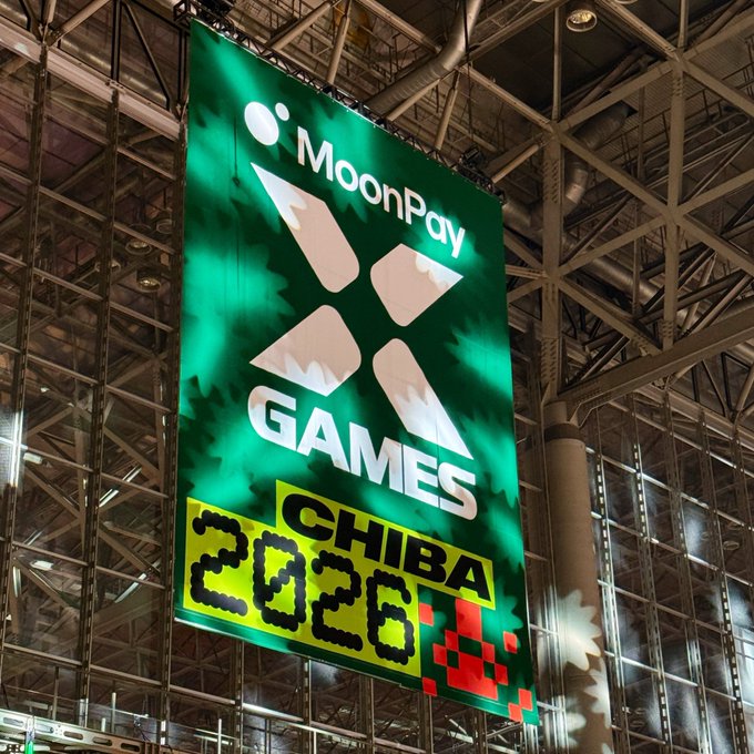 A large banner at MoonPay Games Chiba 2026 hangs from the ceiling of an industrial venue, featuring the MoonPay logo alongside an "X" and pixelated "2026" text that reflects the event's Japan-focused branding.