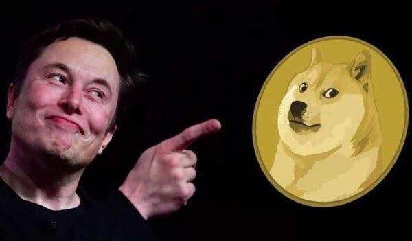 Elon Musk points playfully at a large Dogecoin (DOGE) logo featuring the iconic Shiba Inu dog, visually reinforcing his widely-known association with the cryptocurrency.