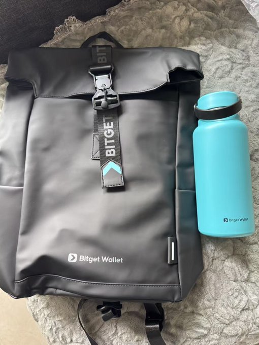 The image features a backpack, a water bottle, and a blue water bottle sitting next to each other on a surface. The backpack appears to be black with a gray lining, while the water bottles are blue. There is also a small amount of text visible in the image that reads "非非非非非非常感谢Bigget送来的入职礼 没想到毕业了还可以用到书包 空间特别大 传统哥哥姐栽培感谢 @kajiweb3 谢谢卡姐栽培感谢 @bitget wallet CN 谢谢一路走来的老师 @solsniper330 @dz_dizzy_dz @aaalyonbtc @luckduckc". The image seems to be related to a post about the importance of staying hydrated and the benefits of using a backpack for carrying items.