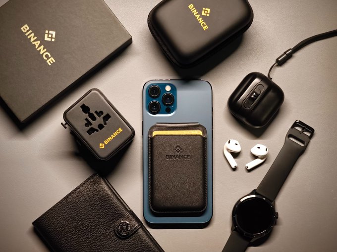 A flat-lay of Binance-branded crypto gear—including a card holder attached to a smartphone, a travel adapter, AirPods, a smartwatch, and a wallet—evokes the "GM Pakistan! Ready to lock in?" vibe of someone geared up and prepared to dive into crypto trading.