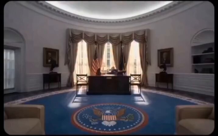 In this image, there is a large circular room with a blue carpet that features a prominent American flag design, and an oval-shaped white room with an ornate ceiling. The room appears to be part of a mansion or a well-decorated office space featuring a desk area, two chairs, and another desk in the background. In addition, there is a painting on display, adding to the overall aesthetic appeal of this lavish setting. The image also contains text that relates to a post about liquidity markets within the predictions marketplace.